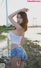 A woman in a white top and denim shorts posing by the water.