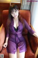 A woman in a purple robe sitting on a brown chair.