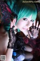 A woman with green hair wearing black gloves and a butterfly headband.