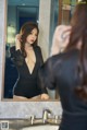 A woman in a black bodysuit looking at herself in the mirror.