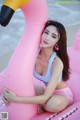 A woman in a bikini sitting on an inflatable flamingo.